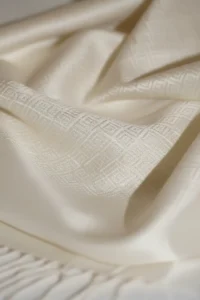 Nærbillede af et hvidt silketørklæde med vævet geometrisk mønster og bløde folder.