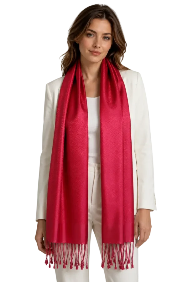 Model iført et langt rødt tørklæde med mønster og frynser forneden, kombineret med hvid blazer og hvide bukser.