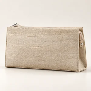 En aflang beige taske med struktur, placeret vandret på et lyst underlag mod en neutral baggrund.