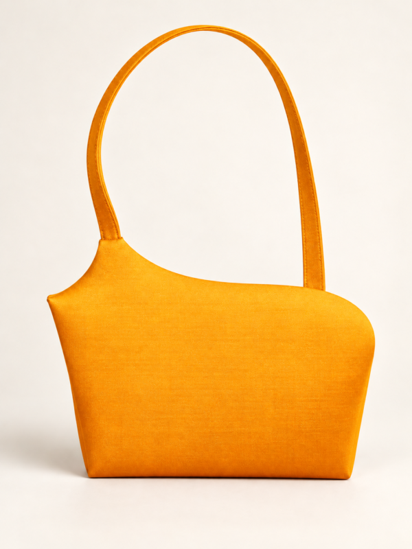 En orange taske med asymmetrisk form og en enkelt hank, fotograferet mod en lys baggrund.